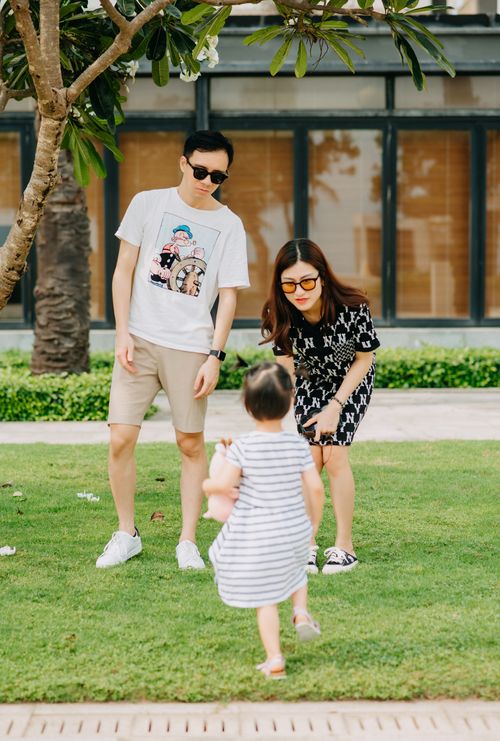Free Full body of trendy mother and father entertaining with small anonymous daughter in striped dress on verdant lawn Stock Photo