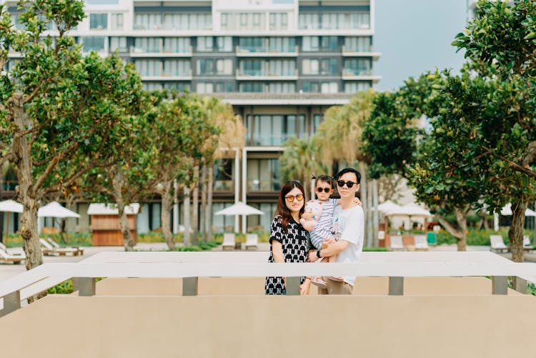 Happy Asian Family On Vacation Near Hotel And Trees