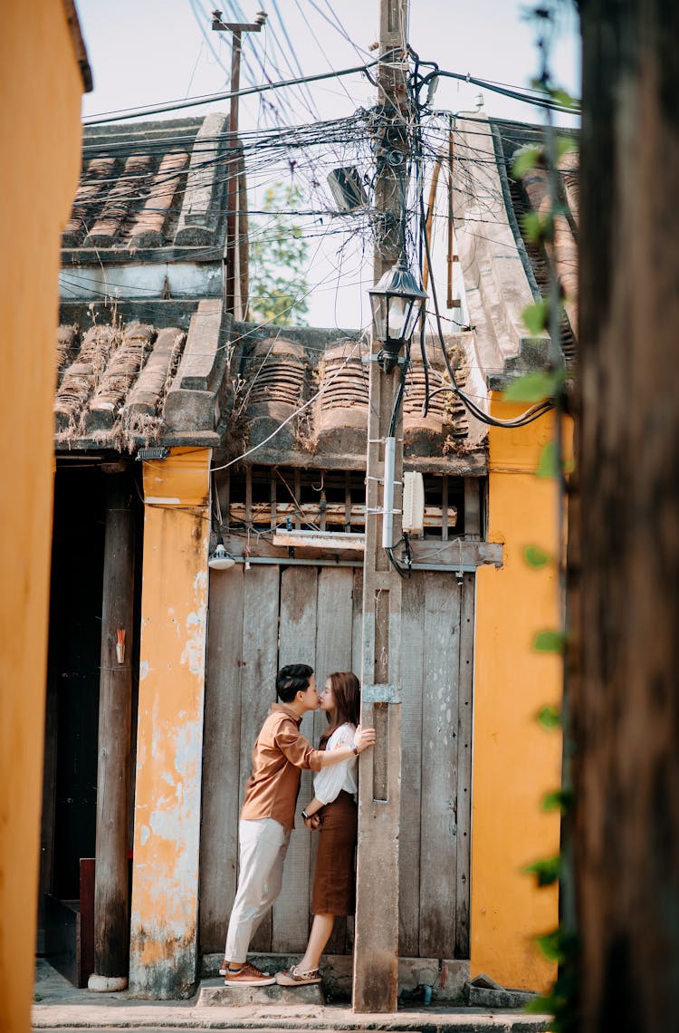 Stylish Young Asian Couple Kissing Near Aged House In Town