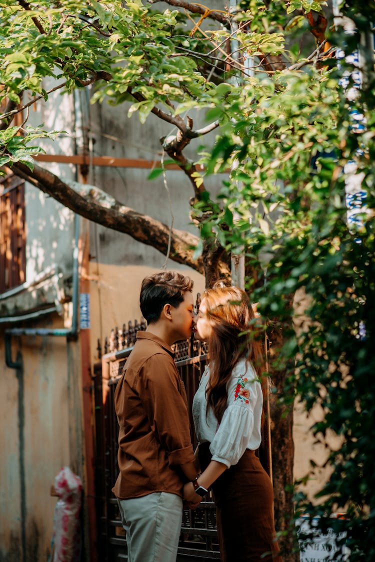 Enamored Young Asian Couple Holding Hands And Kissing On Street In Sunlight