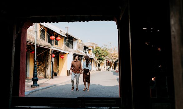 A couple walking hand in hand down a charming Asian street with traditional lanterns.