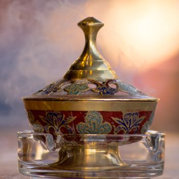 Ornate brass incense burner with intricate floral designs emitting gentle smoke, ideal for traditional decor.