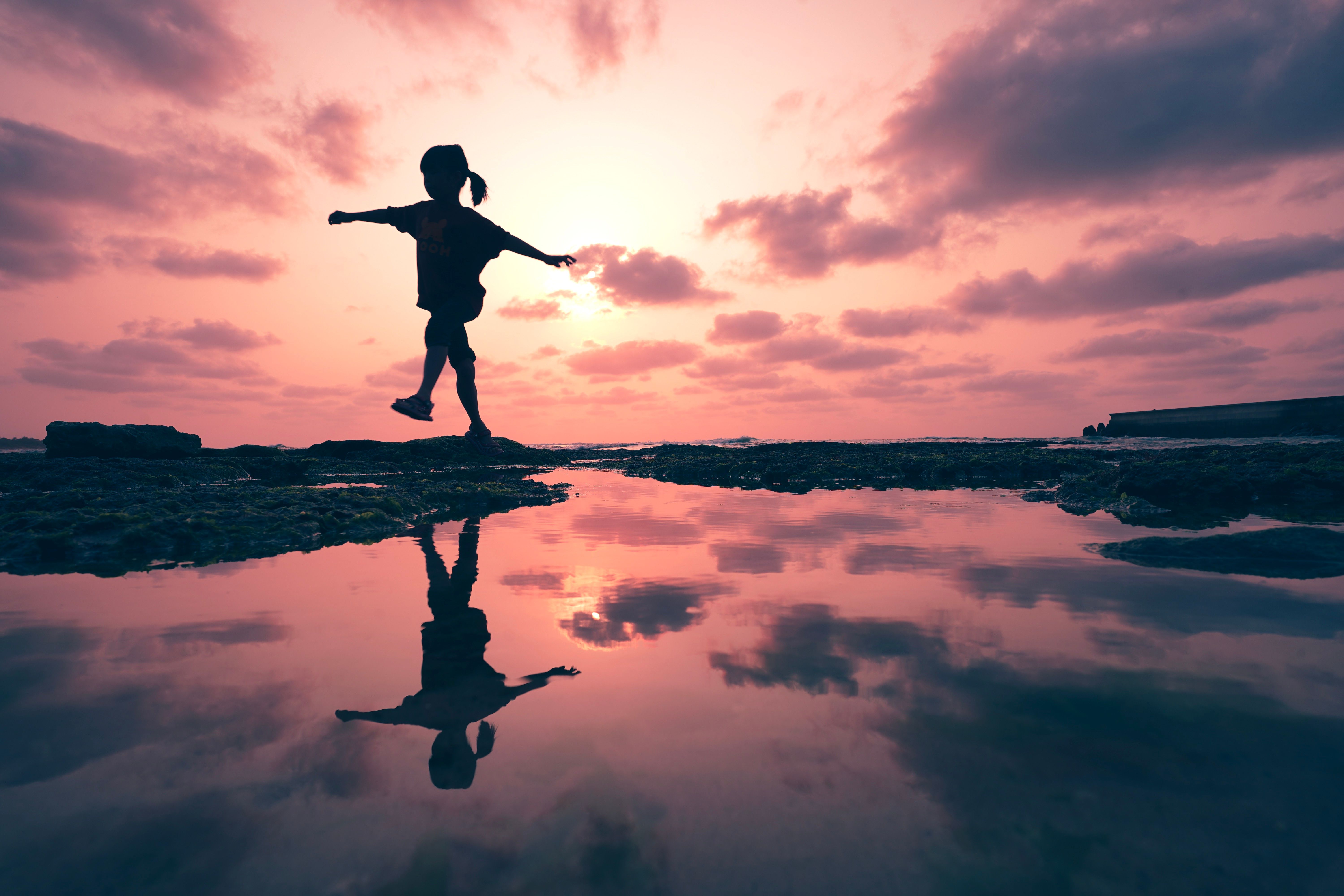 A Gril Walking Near a Body of Water at Sunset · Free Stock Photo