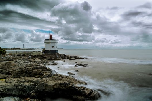 White Lighthouse on Rocky Shore Under White Clouds