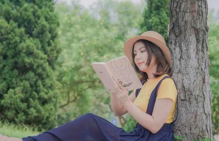 Girl Leaning On Brown Tree Trunk Reading Book