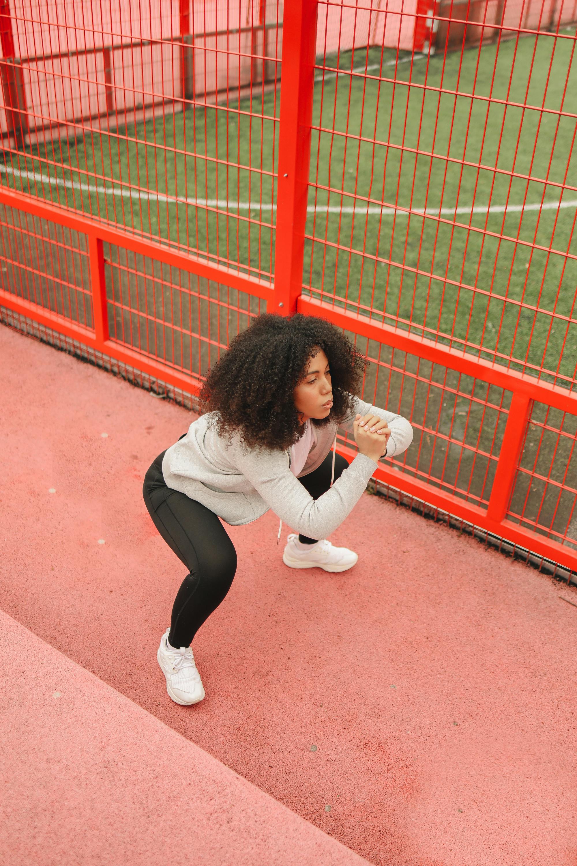 Woman performing squats on a vibrant red sports track, emphasizing fitness and healthy lifestyle.