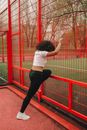 Woman in White Crop Top and Black Leggings Exercising Beside a Red Steel Fence