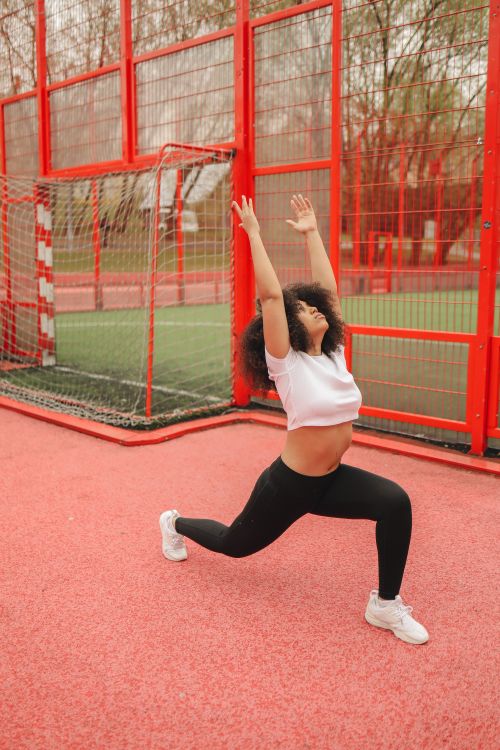 Free Young woman performing a stretch exercise at a vibrant red outdoor sports court. Stock Photo