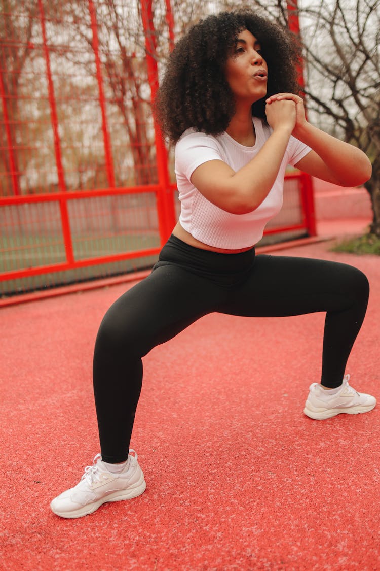 A Woman In White And Black Sportswear Doing Sumo Squats