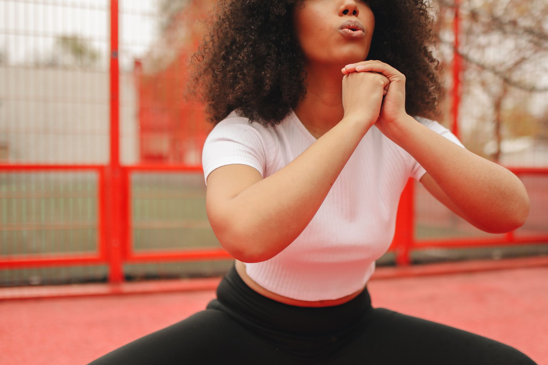 Focused woman performing squats outdoors in a white shirt and black leggings, showcasing fitness and determination.