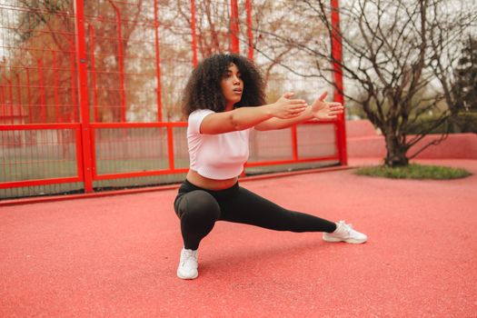 Woman in athletic wear stretching outdoors on a red track, promoting fitness and wellness.
