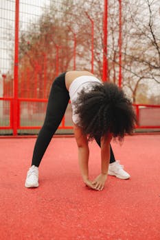 An African American woman stretching in a vibrant outdoor sports court, embracing a healthy lifestyle.
