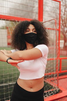 African American woman wearing a mask, stretching outdoors during a fitness routine.