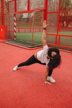 A woman in activewear stretches on a vibrant red sports court, promoting fitness and health.