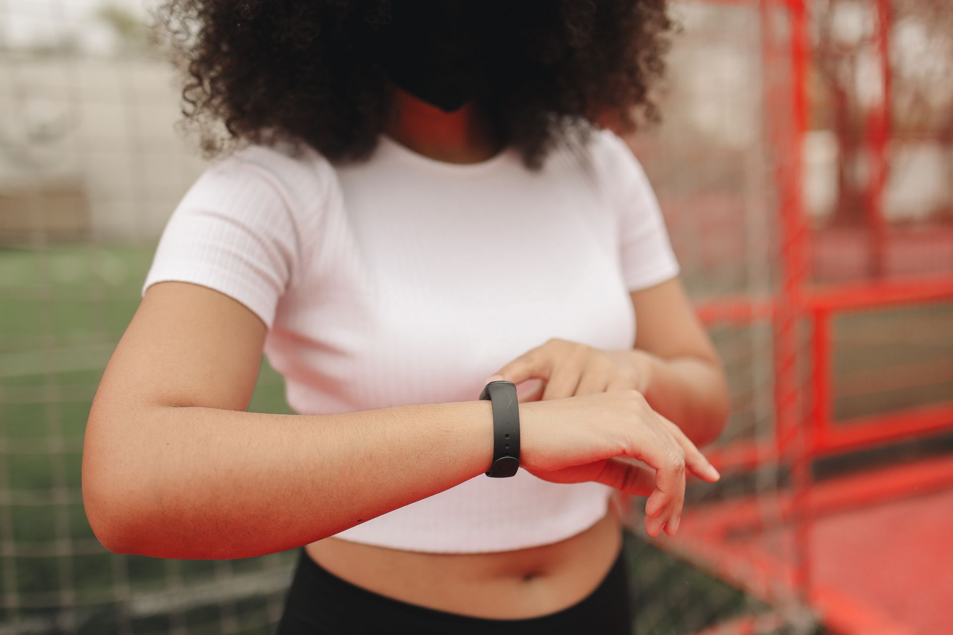 Young woman wearing a fitness tracker, checking time in an outdoor sports area.