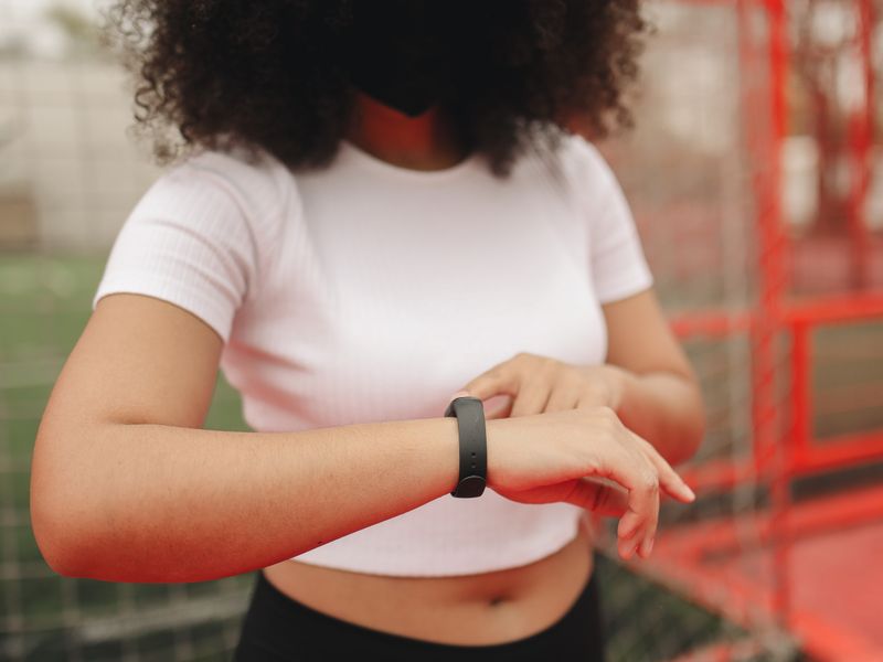 Young woman wearing a fitness tracker, checking time in an outdoor sports area.