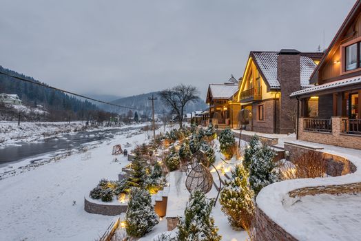 Charming winter resort with cozy cottages by a snowy riverside, perfect for relaxation.