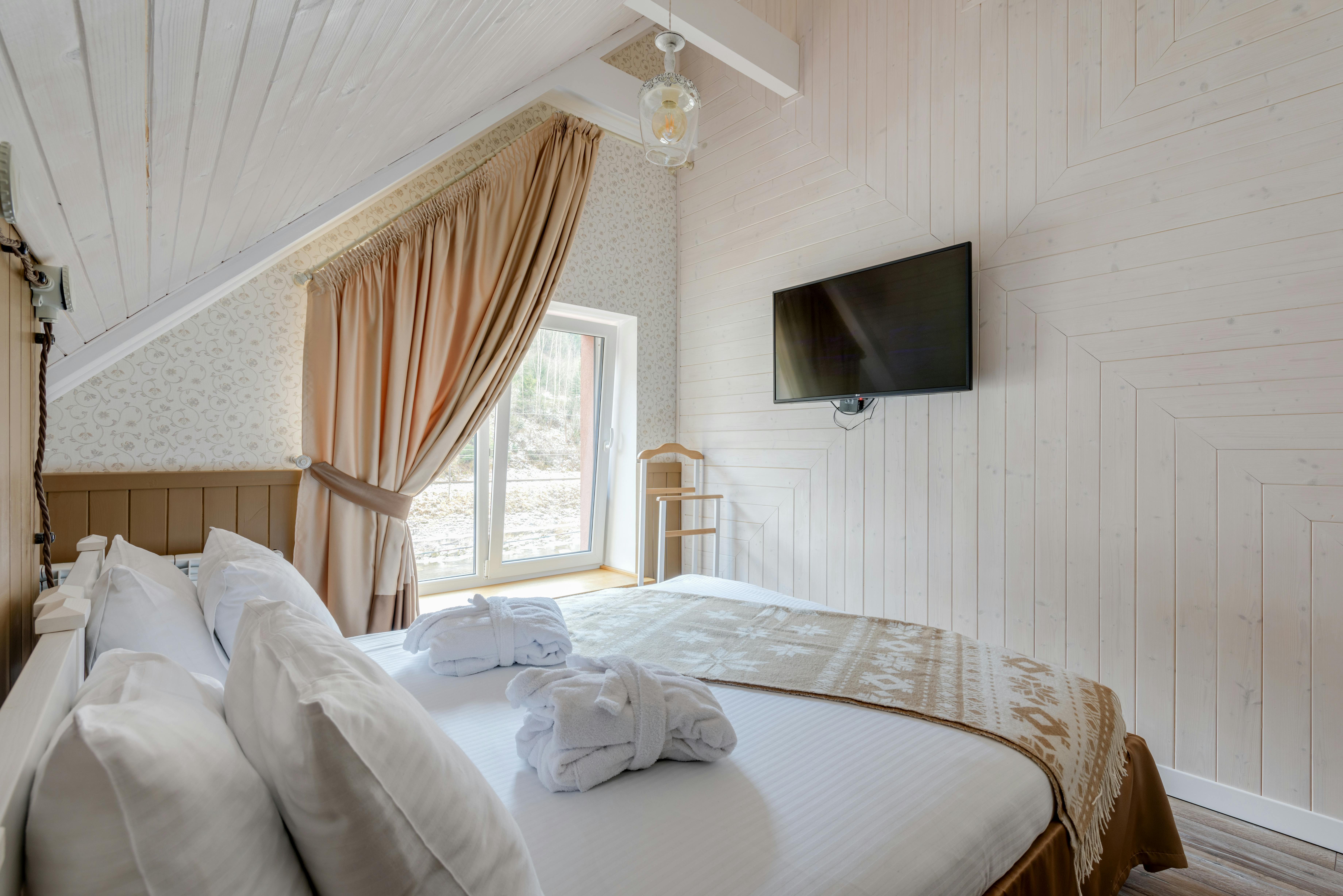 Cozy attic bedroom featuring modern decor with a wall-mounted TV and elegant linens.