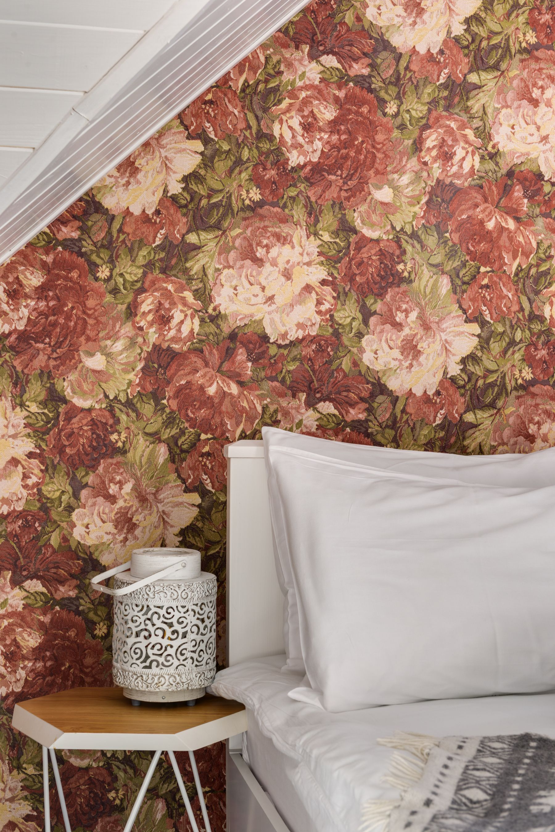 White bed and simple bedside table against deep rose botanical wallpaper