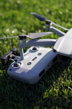 Close-up of a sleek drone and controller resting on vibrant green grass.