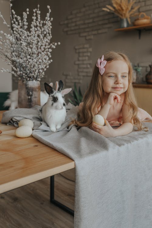 Adorable girl lying on table with rabbit and Easter eggs