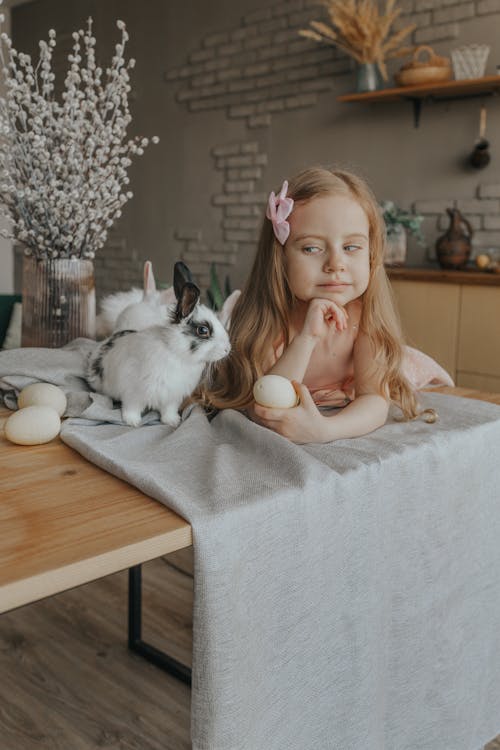 Charming girl at table with bunnies and Easter eggs