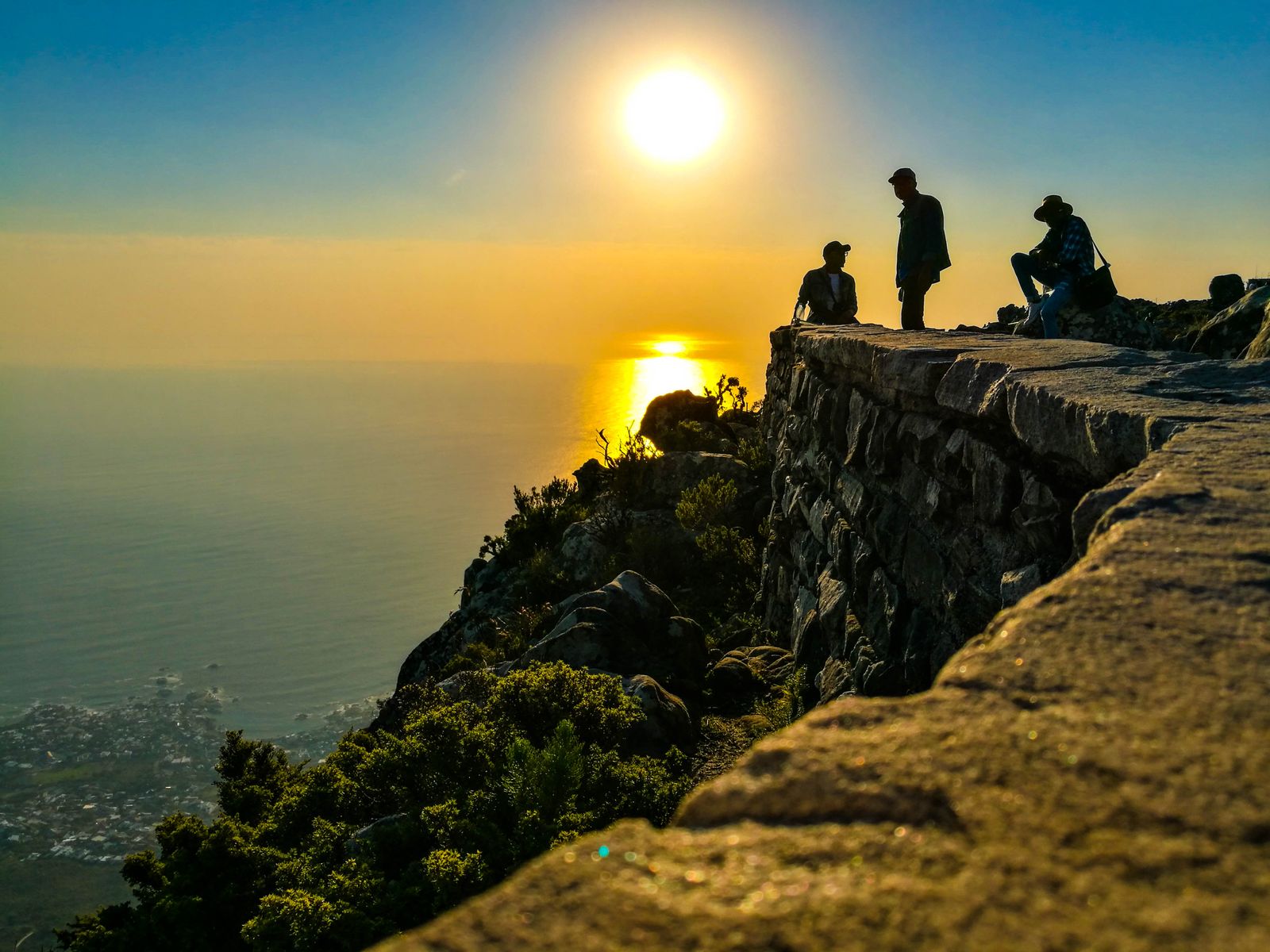 A person sitting at a clifftop edge as the sun sets over the ocean.