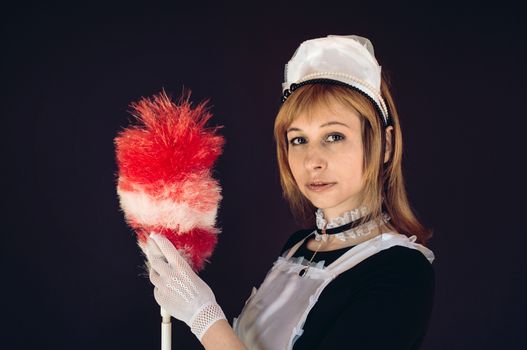 Charming female wearing costume of cleaning lady with tool for dusting looking at camera