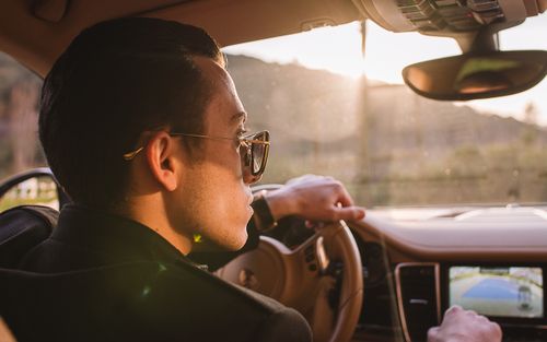 Free Man driving luxury car at sunset wearing sunglasses, showcasing elegant car interior and confident style. Stock Photo