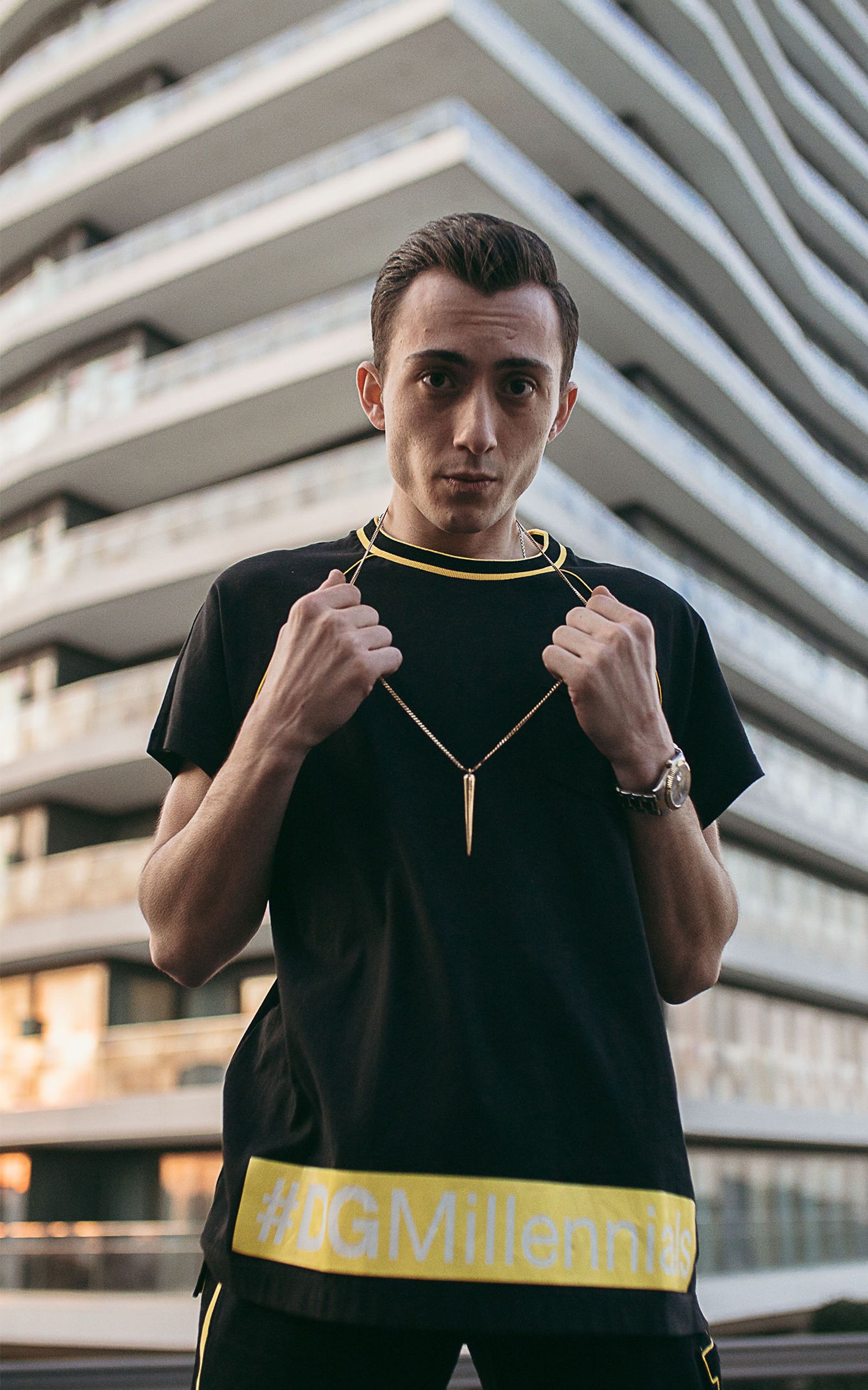 Stylish young man in black shirt with a necklace in an urban setting.