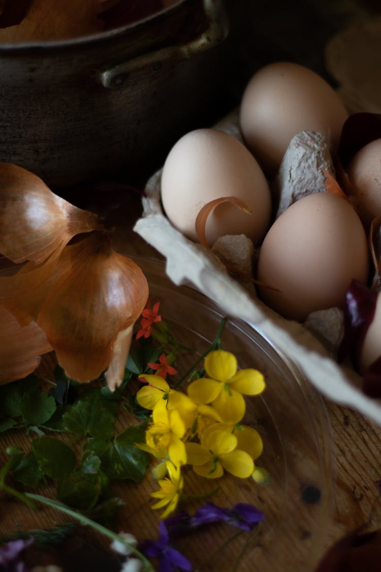 Eggs In Box With Onion Skin And Flowers On Table