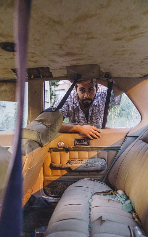 Free Man peering into a weathered car interior, sunlight highlighting the worn details Stock Photo