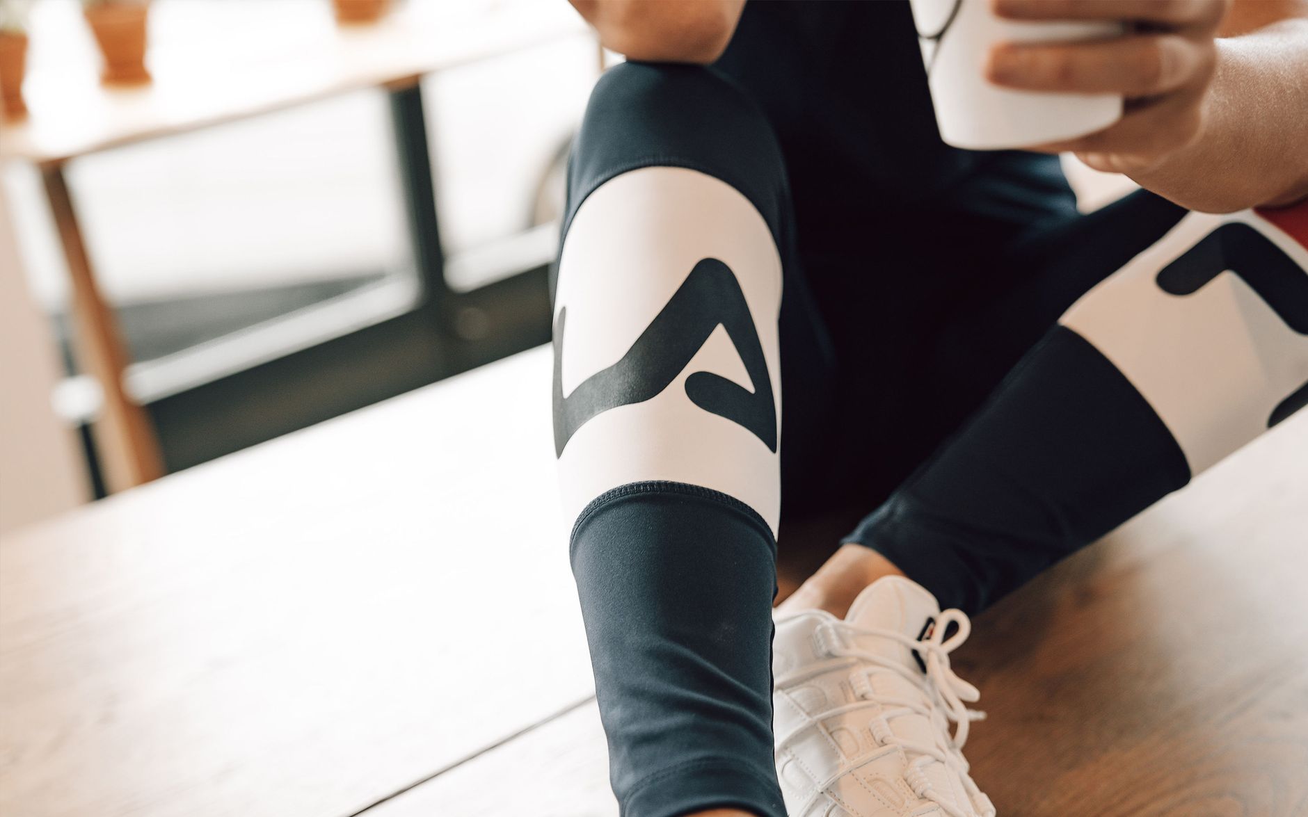 A person wearing stylish athletic leggings and sneakers sitting indoors, holding a smartphone.