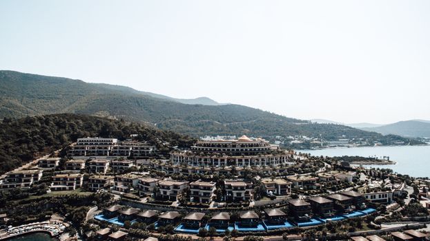 Aerial view of a luxurious resort nestled in lush hills by the sea, showcasing modern architecture.