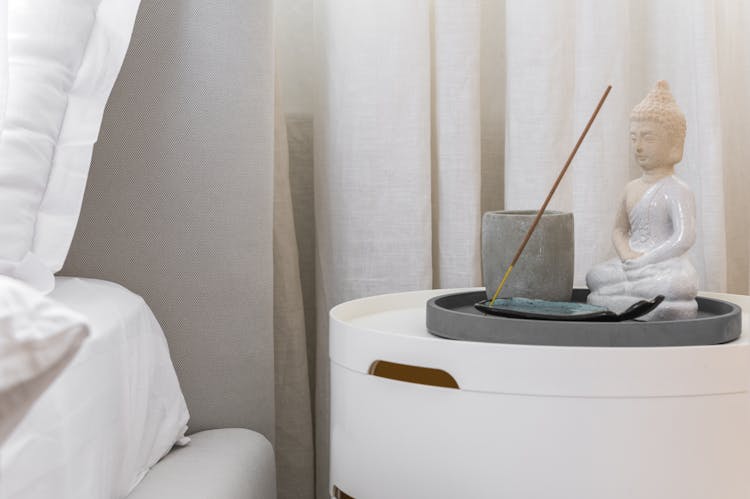 White Buddha Statue And Incense By A Bed