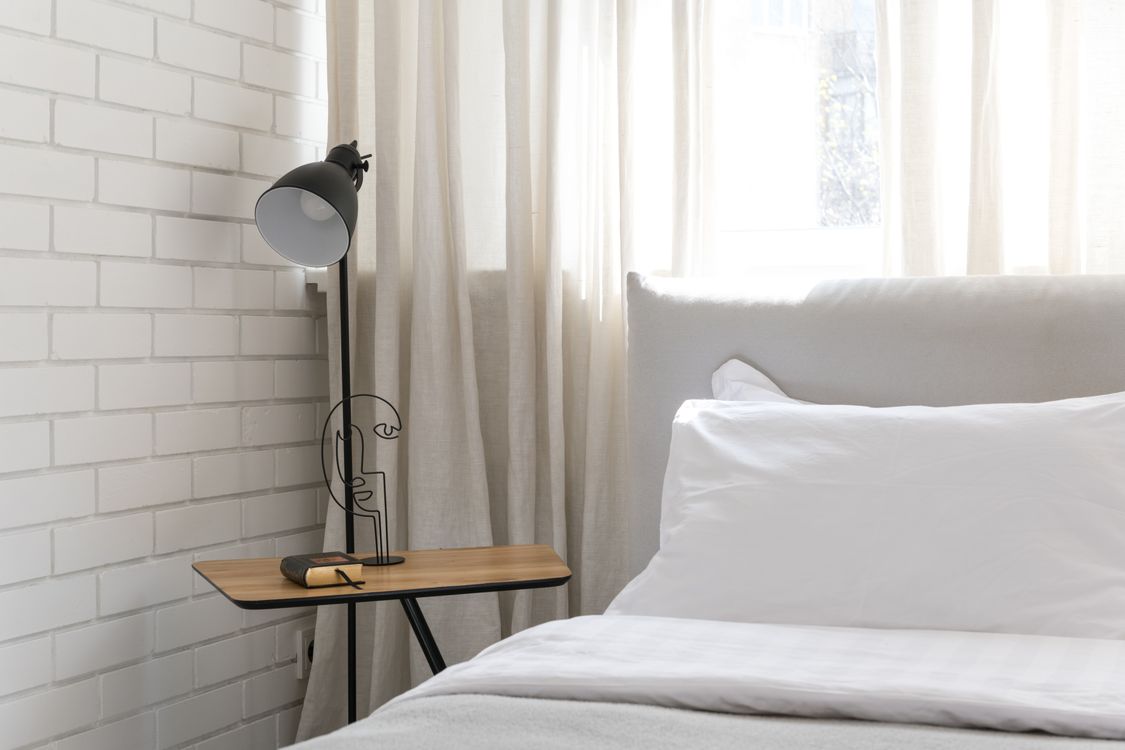 Minimal bedroom with stylish bedside table lamp — layered lighting in rental apartment decor