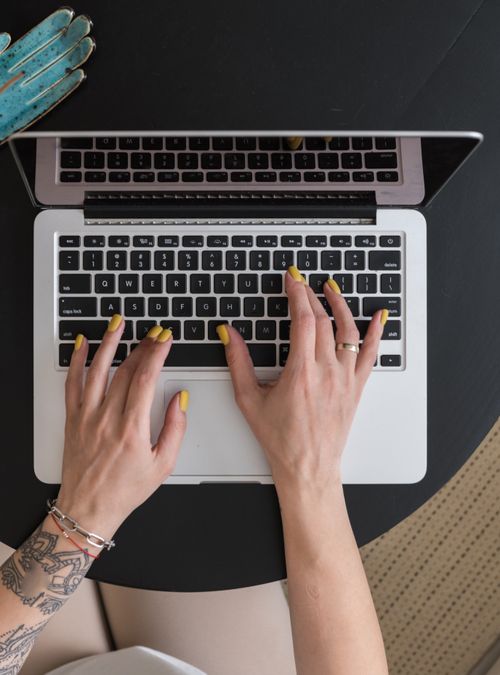 Free Close-up of hands with yellow manicured nails typing on a laptop keyboard from an overhead angle. Stock Photo