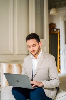 Caucasian man in a suit focused on work with a laptop in an elegant indoor setting.
