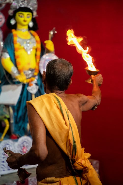 Man in Yellow Traditional Clothing Holding Fire in front of Statue