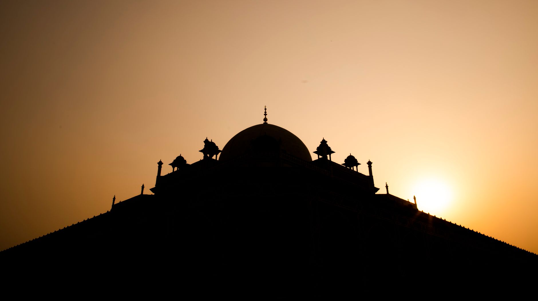 New Delhi skyline at sunrise with India Gate, busy roads, and warm golden haze