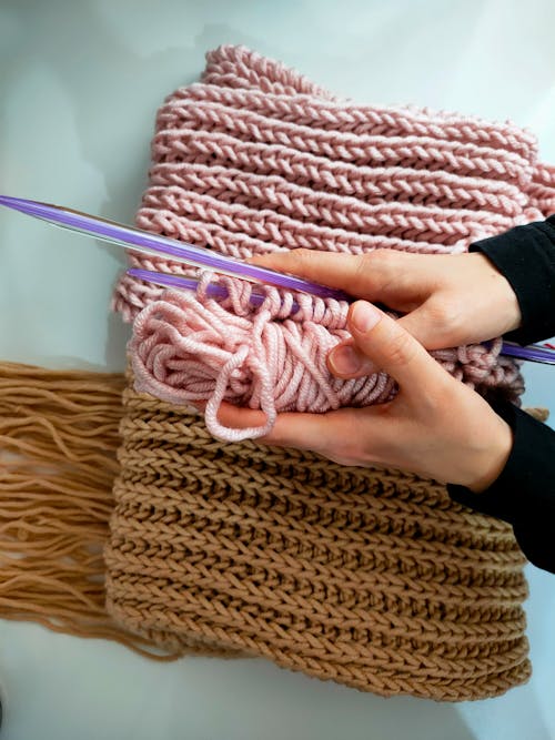 Close-Up Photo of a Person's Hands Holding Knitting Needles and a Pink Yarn