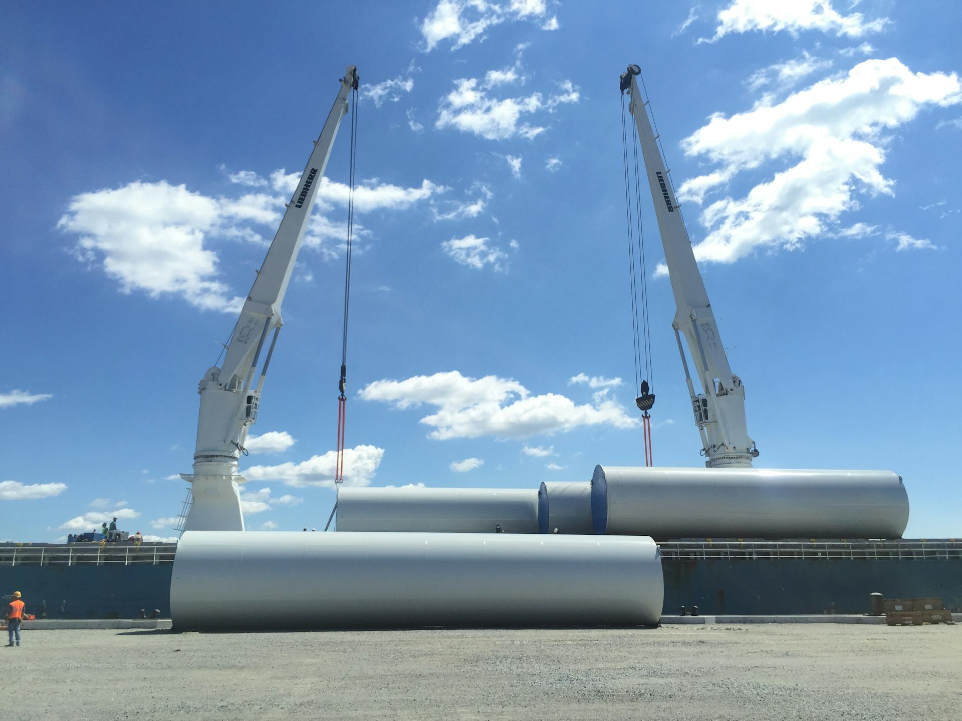 Crane loading large metal cylinders at New Bedford port under clear skies.