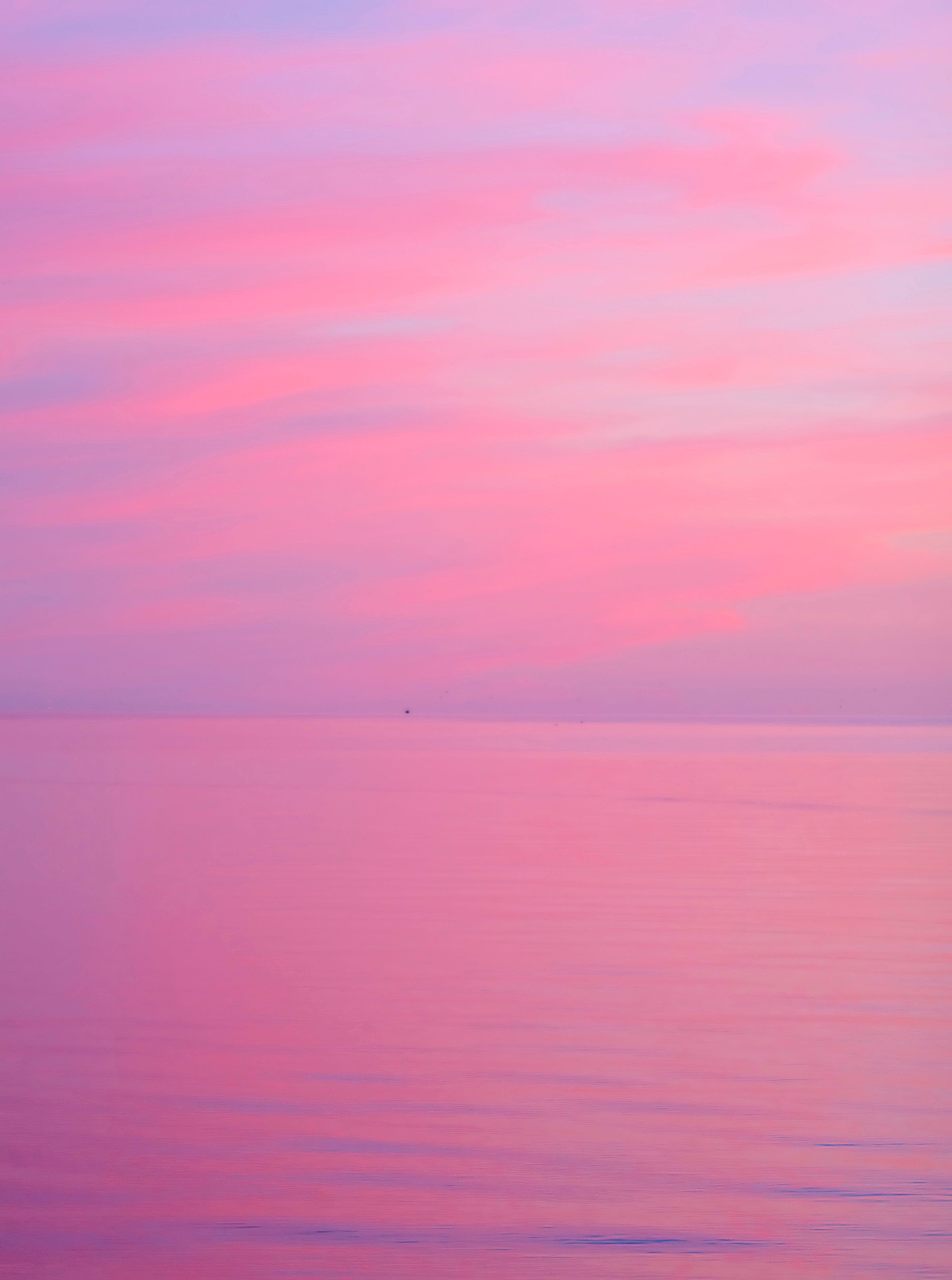Serene pink pastel dawn sky reflecting over a calm sea, creating a tranquil seascape.
