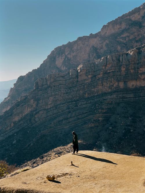 Free Distant anonymous person standing on edge of steep rock above rough mountain ridge against blue sky in sunny highland area Stock Photo