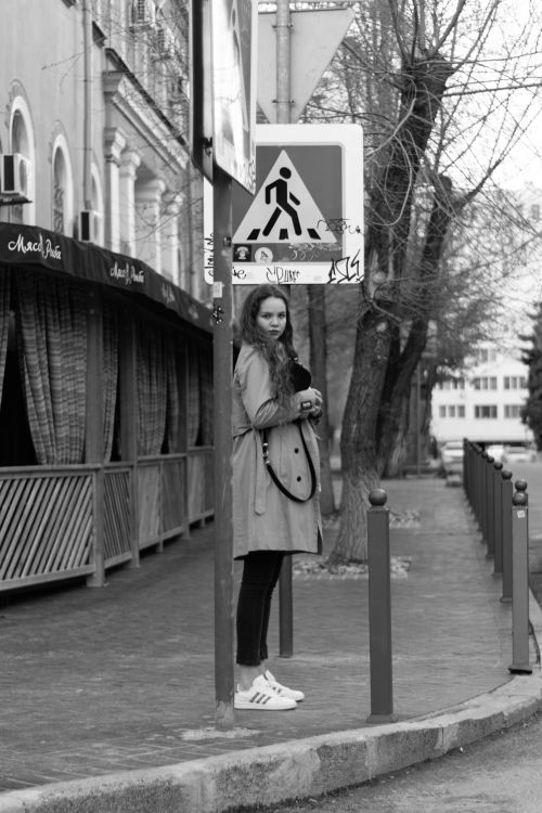Free A woman stands near a street sign on a city sidewalk, in black and white. Stock Photo
