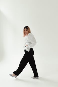 Fashionable Asian woman in black pants and white shirt posing in a studio setting.