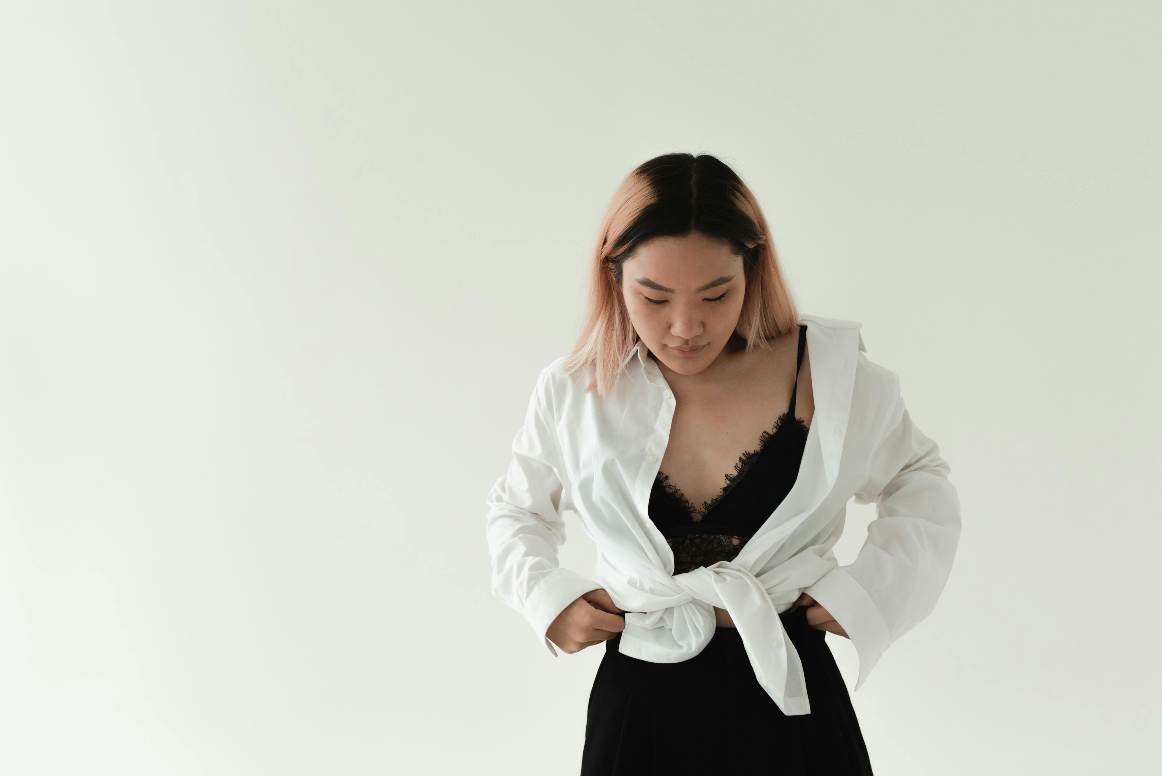 Adult Asian woman in white shirt with black lace top, minimalist fashion, neutral background.