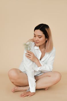 A tranquil portrait of a woman sitting and holding flowers, wearing a white shirt.