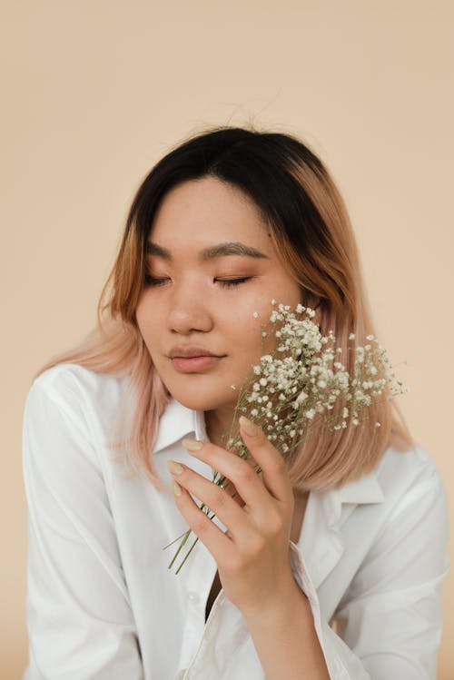 Close-Up Shot of a Pretty Woman in White Long Sleeves Holding Flowers