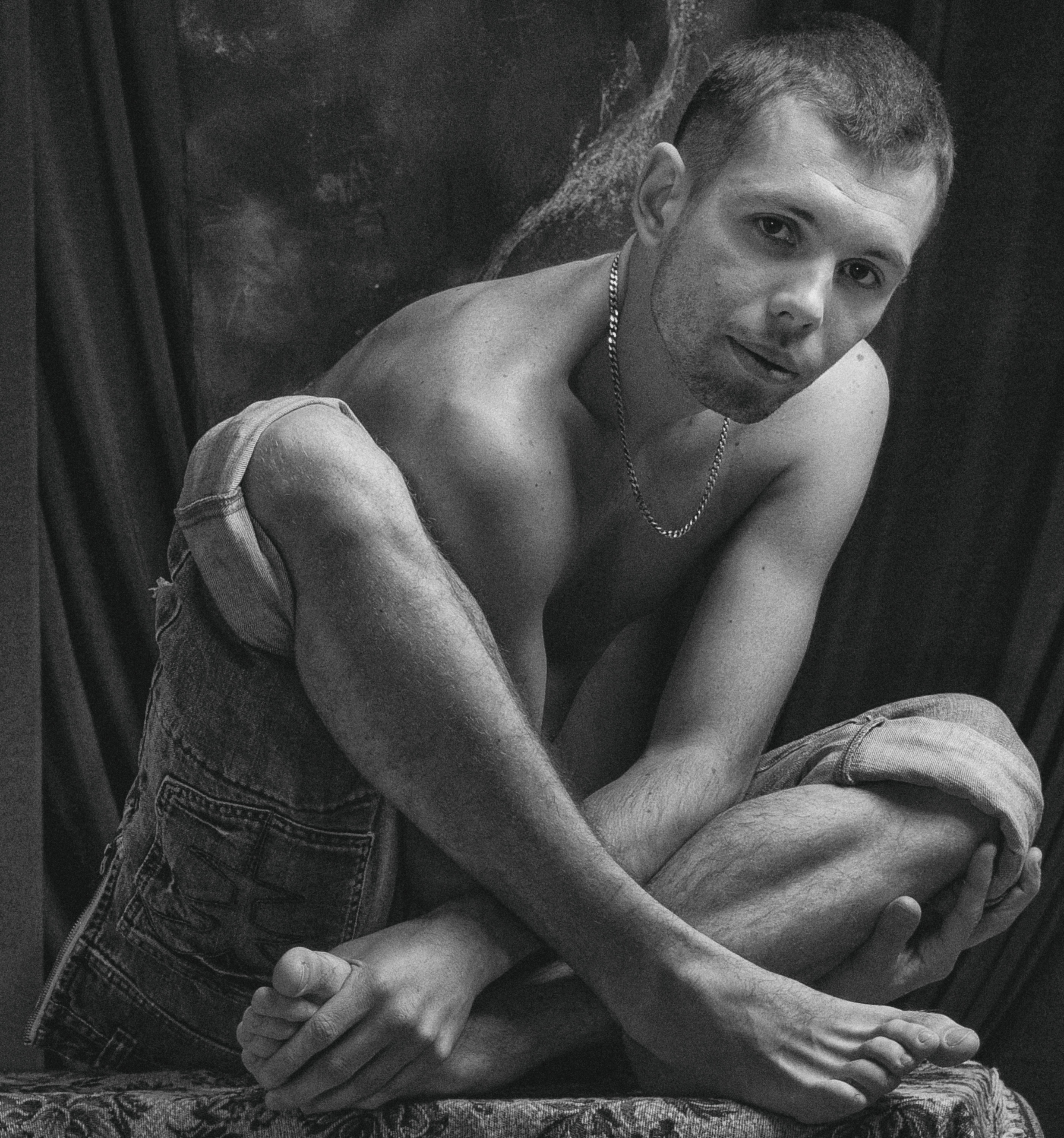 Artistic black and white portrait of a shirtless man posing in denim shorts.